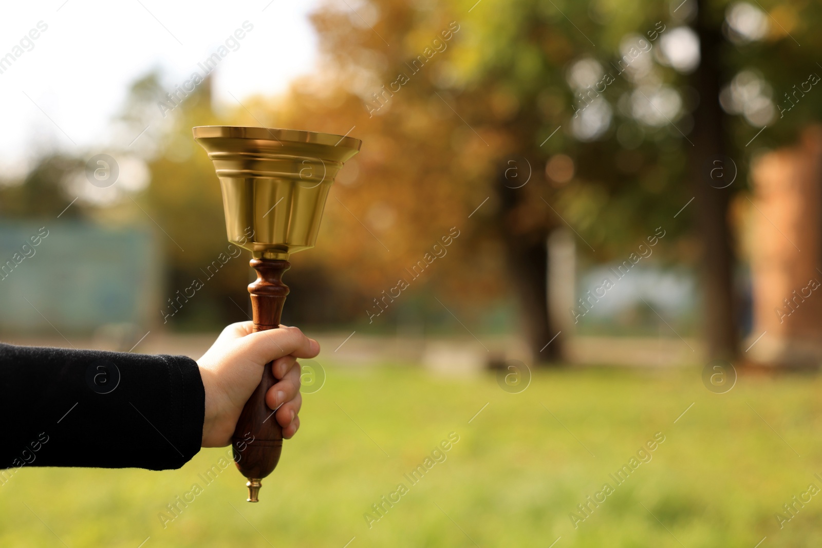 Photo of Pupil holding school bell outdoors on sunny day, closeup. Space for text