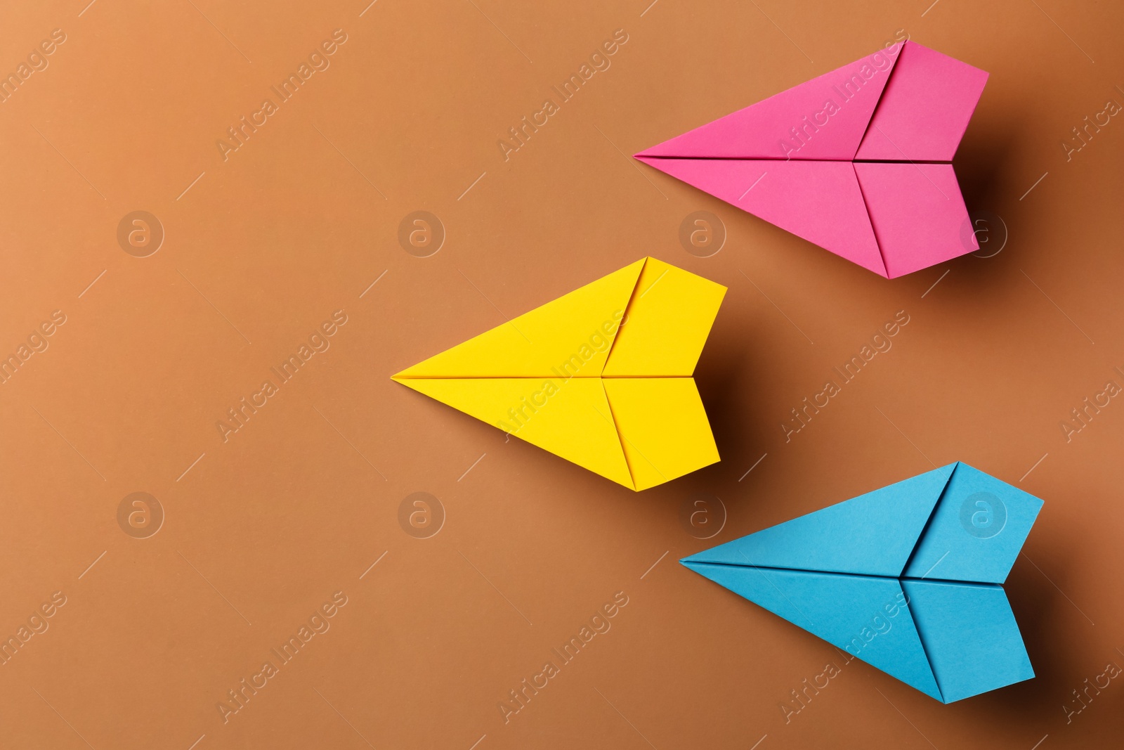 Photo of Handmade colorful paper planes on brown background, flat lay. Space for text