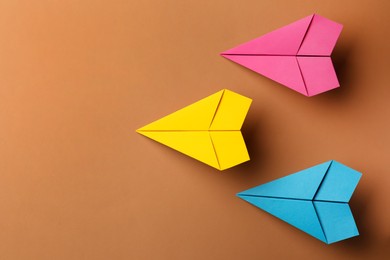 Handmade colorful paper planes on brown background, flat lay. Space for text