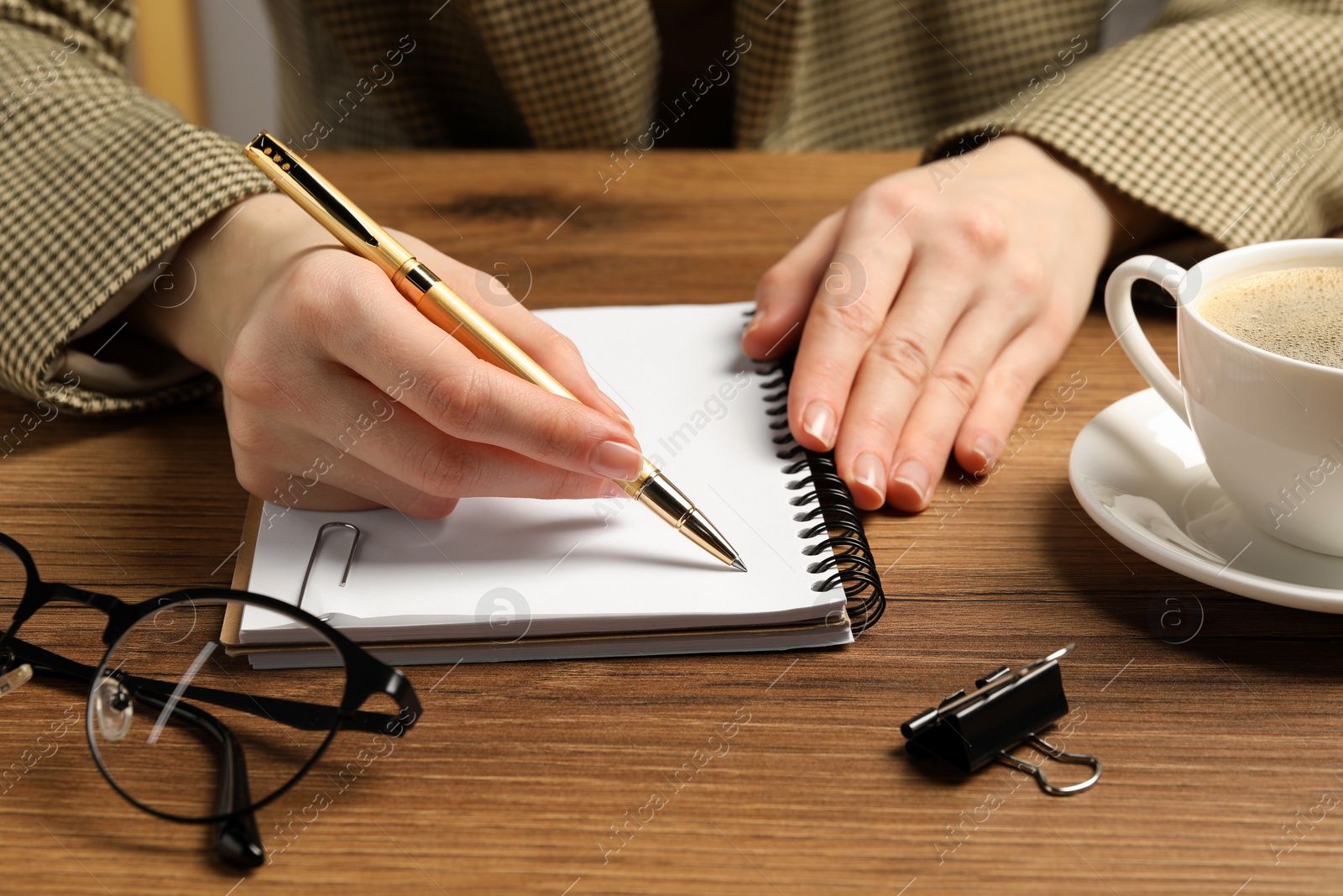 Photo of Woman writing in notebook at wooden table, closeup