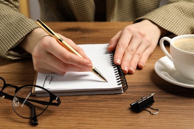 Woman writing in notebook at wooden table, closeup