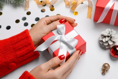 Woman holding gift box near Christmas decor on white background, closeup