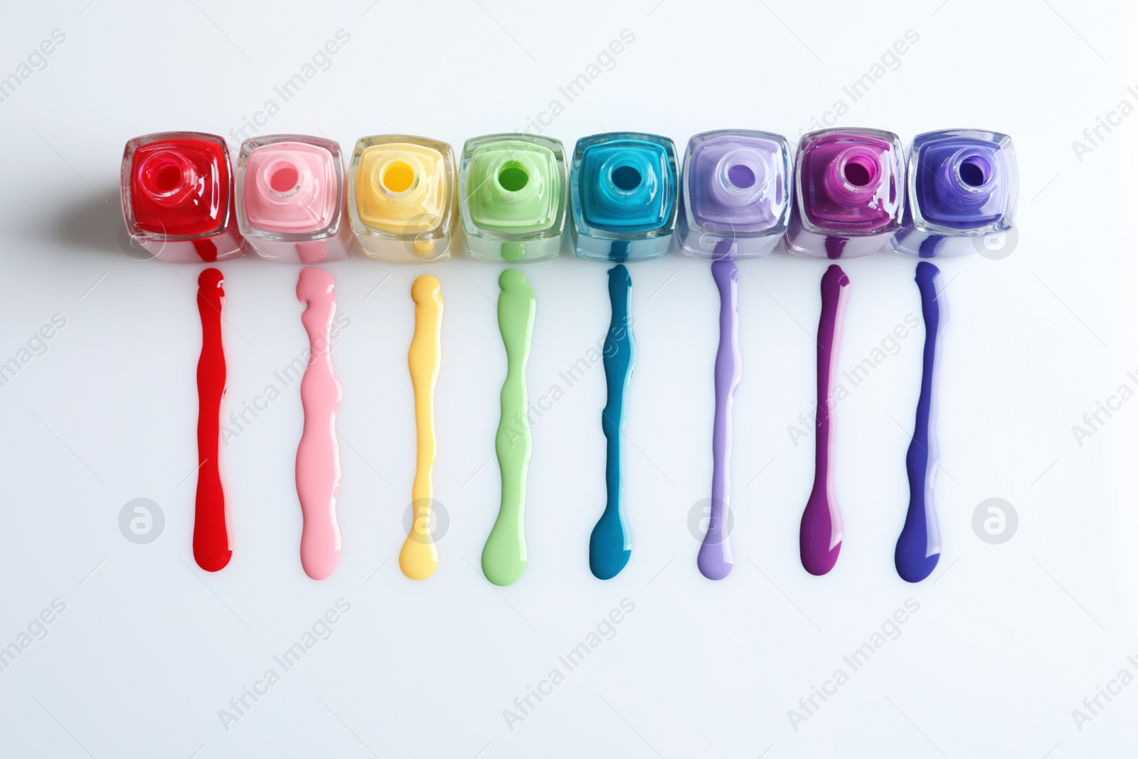 Photo of Spilled colorful nail polishes and bottles on white background, top view