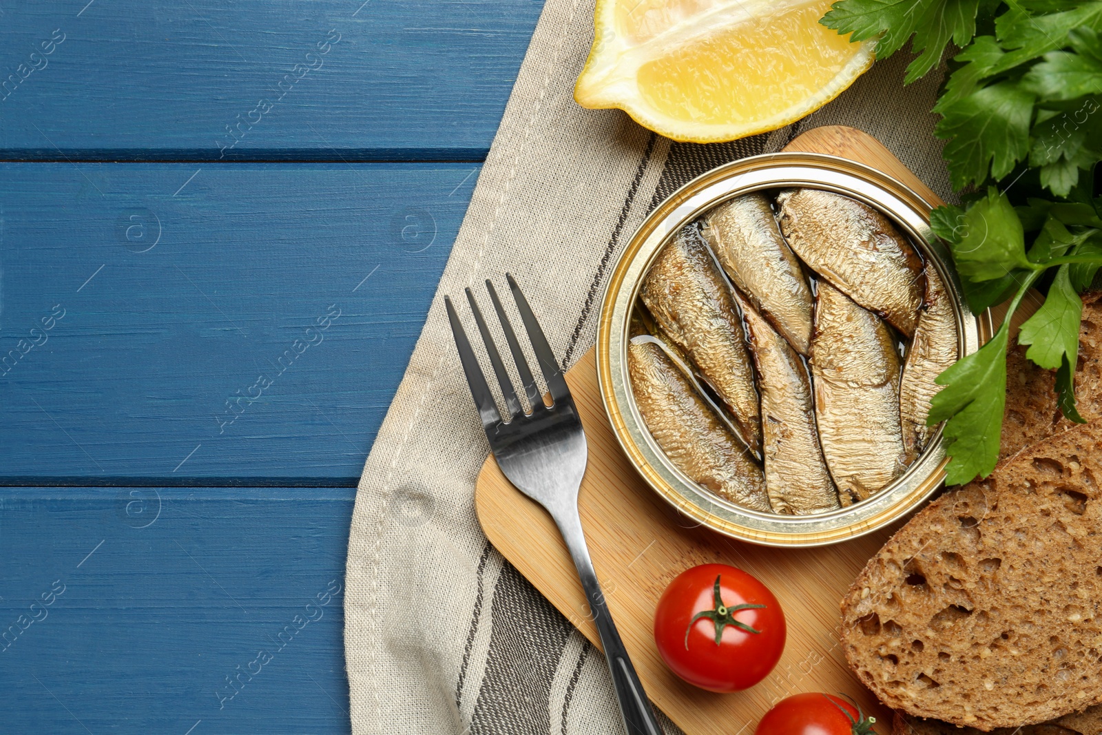 Photo of Tin can with tasty sprats served on blue wooden table, flat lay. Space for text