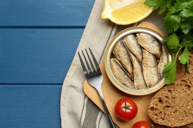 Photo of Tin can with tasty sprats served on blue wooden table, flat lay. Space for text