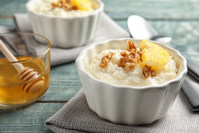 Photo of Creamy rice pudding with walnuts and orange slice in ramekin served on wooden table