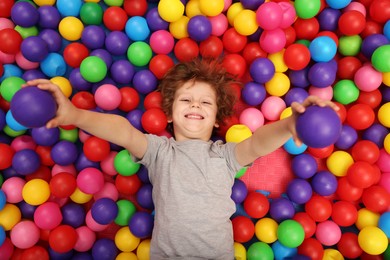 Happy little boy lying on many colorful balls, top view