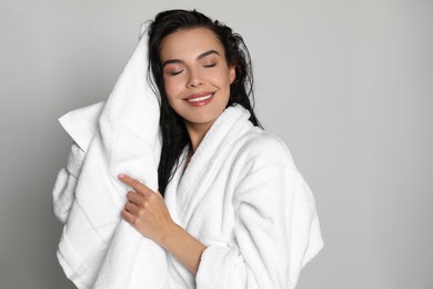 Photo of Beautiful young woman in bathrobe drying hair with towel on light background