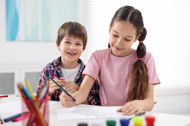 Photo of Happy brother and sister drawing at white table in room