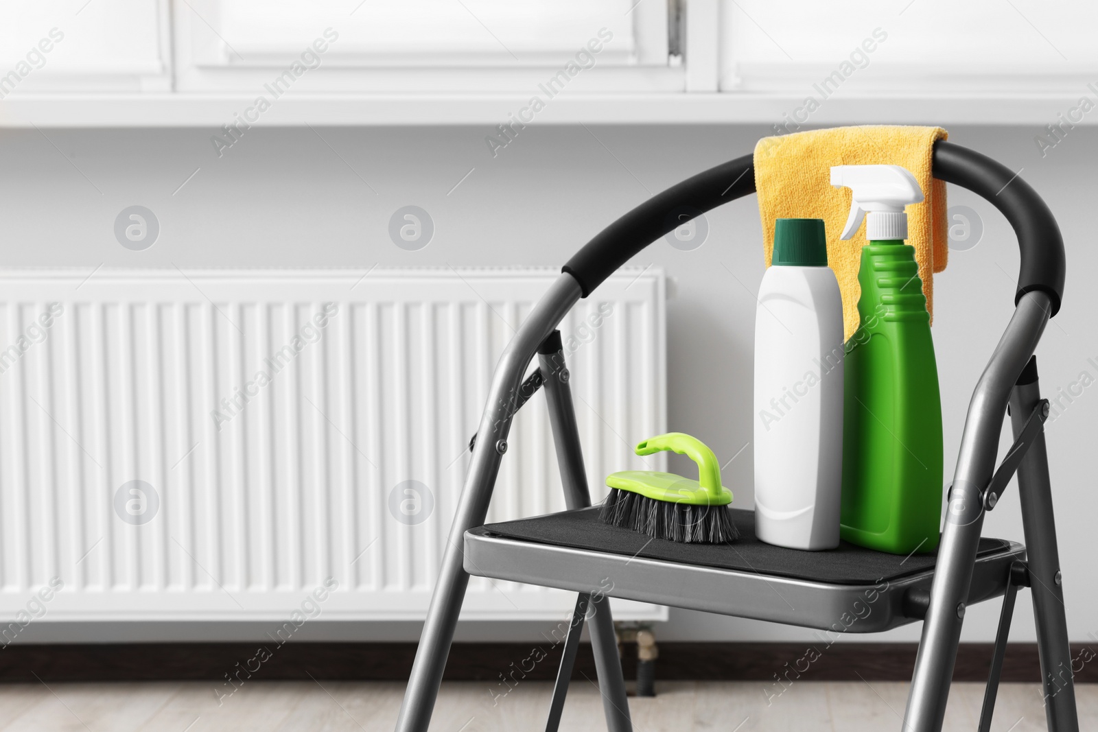 Photo of Ladder with cleaning supplies near modern radiator in room