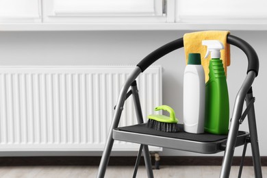 Photo of Ladder with cleaning supplies near modern radiator in room