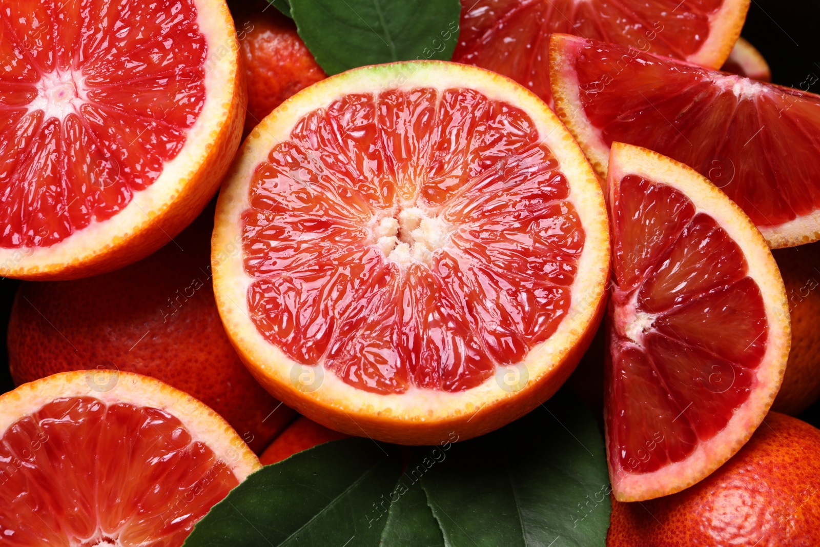 Photo of Slices of fresh ripe red orange with green leaves as background, closeup