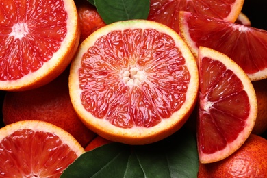 Slices of fresh ripe red orange with green leaves as background, closeup