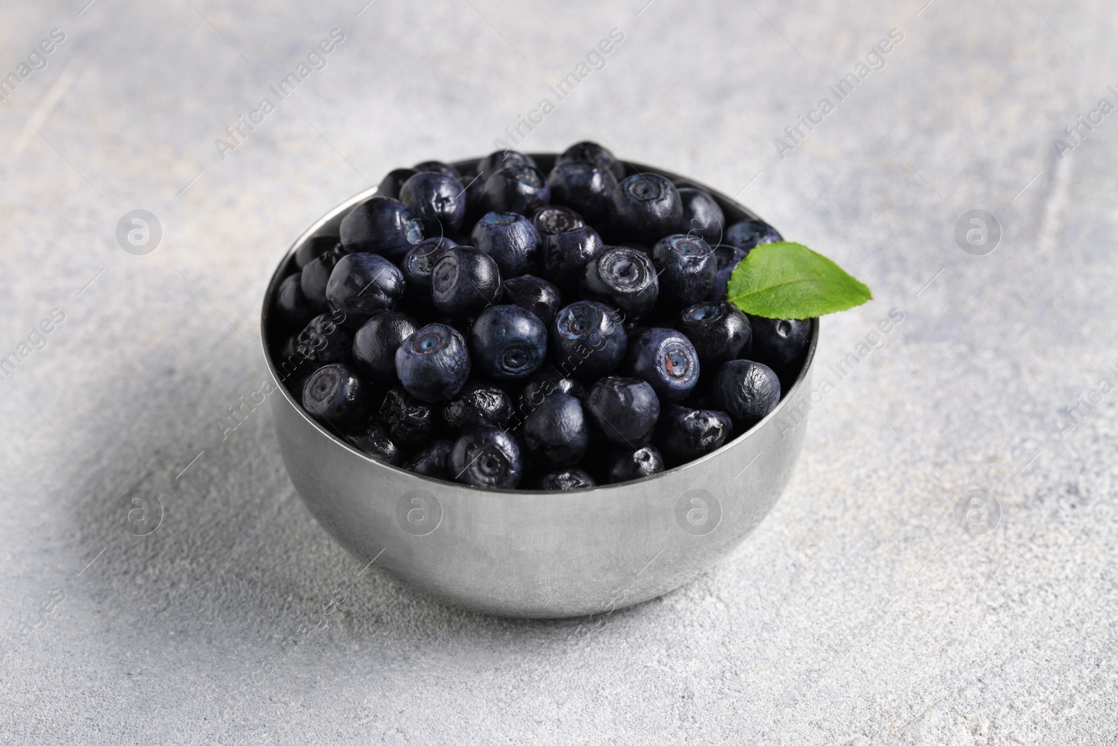 Photo of Ripe bilberries and leaf in bowl on light grey textured table