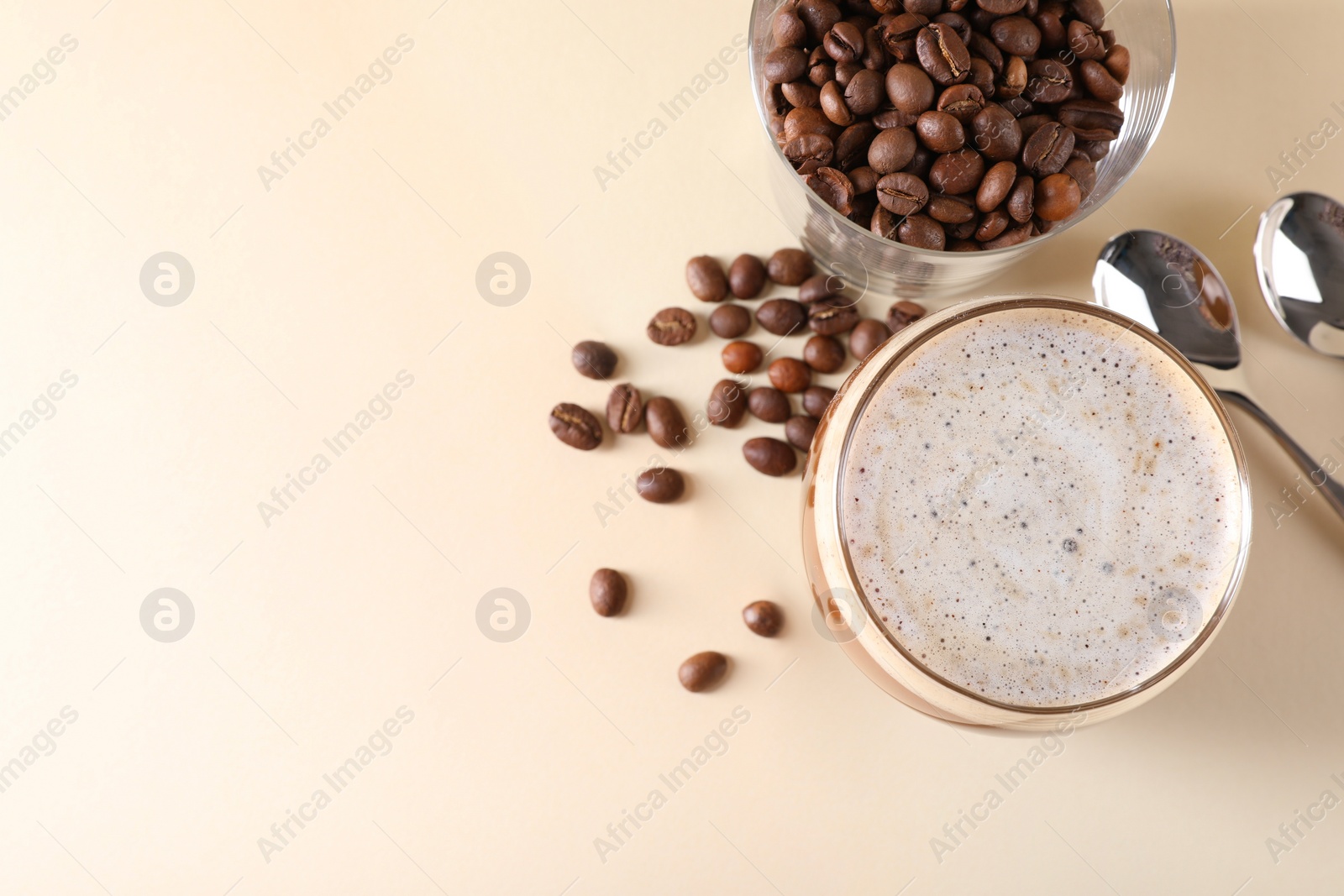 Photo of Refreshing iced coffee with milk in glass, beans and spoons on beige table, flat lay. Space for text