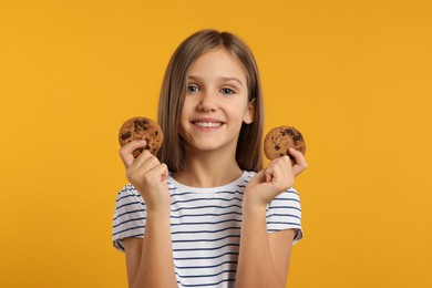 Cute girl with chocolate chip cookies on orange background