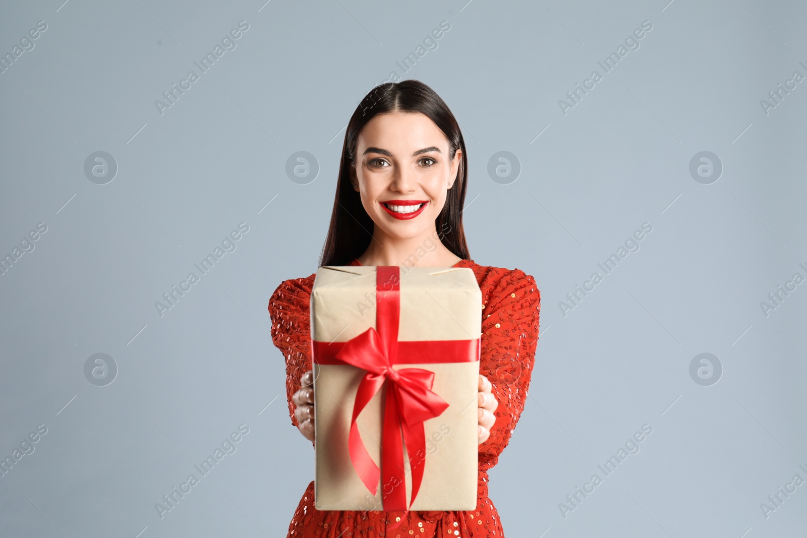 Photo of Woman in red dress holding Christmas gift on grey background