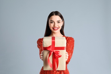 Photo of Woman in red dress holding Christmas gift on grey background