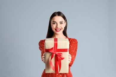 Woman in red dress holding Christmas gift on grey background