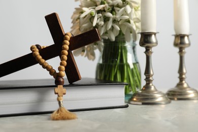 Wooden cross, rosary beads, Bible, church candles and flowers on light table