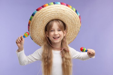 Photo of Cute girl in Mexican sombrero hat with maracas on purple background