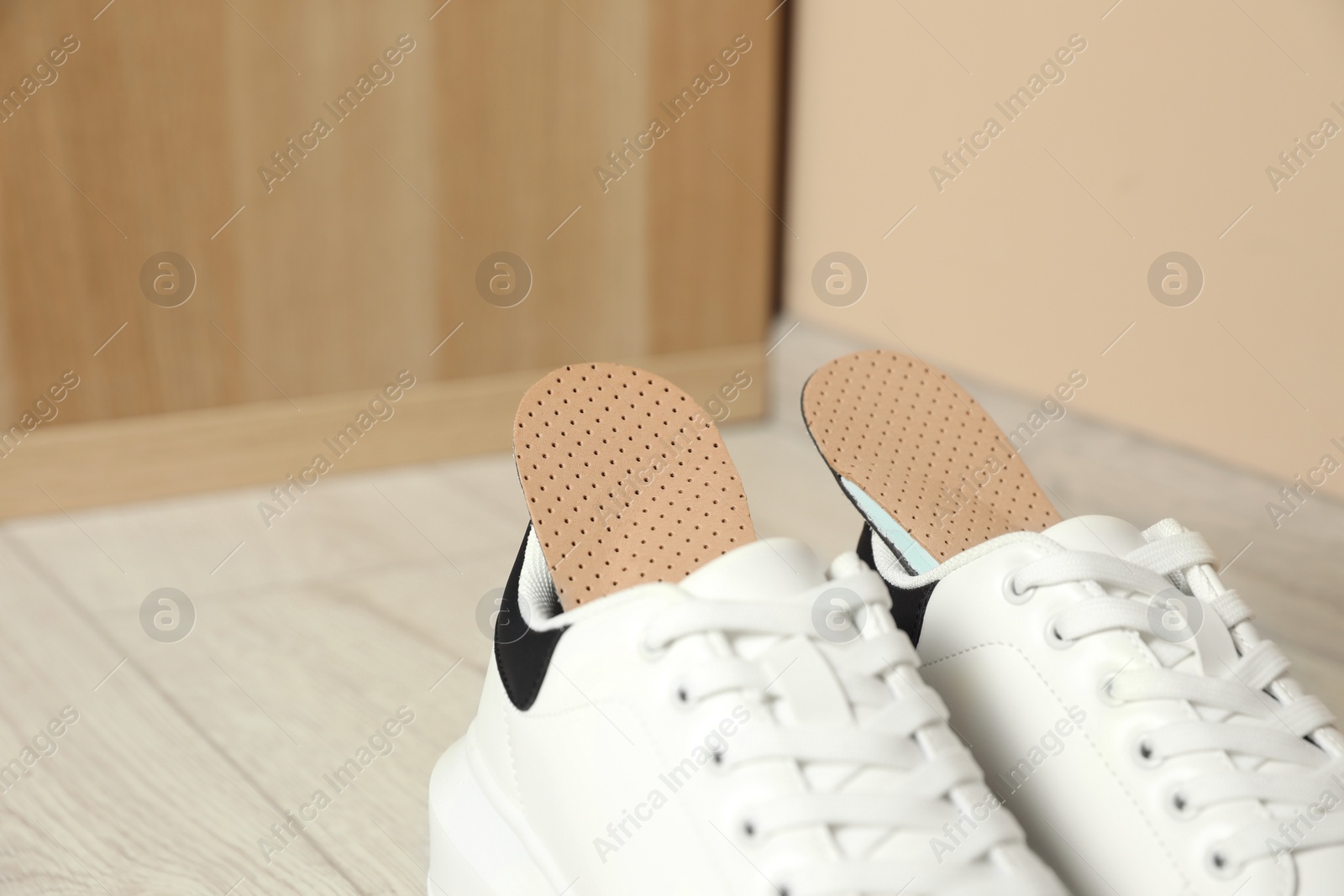 Photo of Orthopedic insoles in shoes on floor, closeup. Space for text