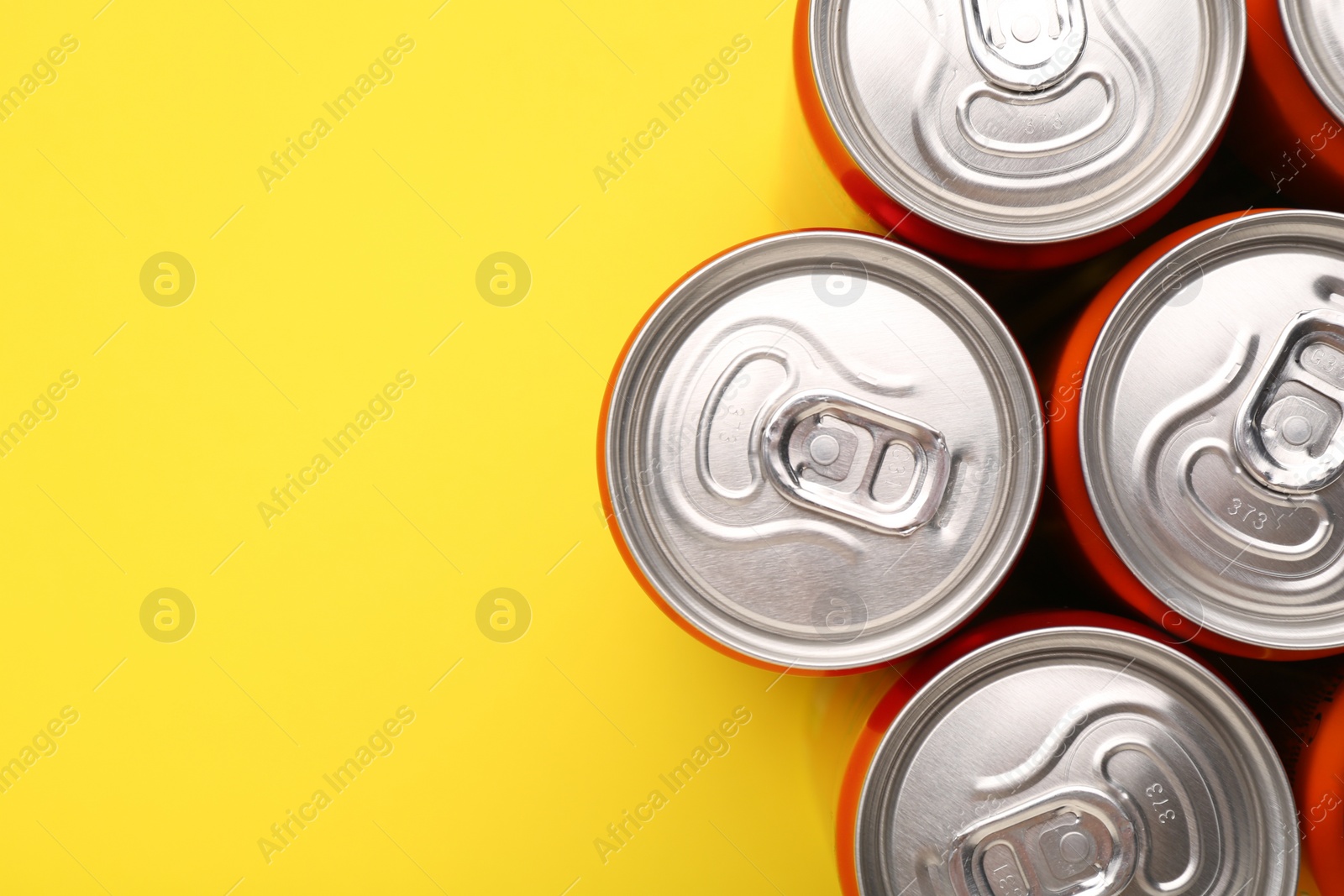 Photo of Energy drink in cans on yellow background, top view. Space for text