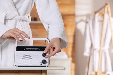 Photo of Woman in bathrobe turning volume knob on radio indoors, closeup. Space for text