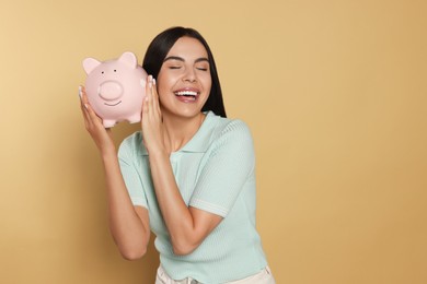 Happy young woman with ceramic piggy bank on beige background