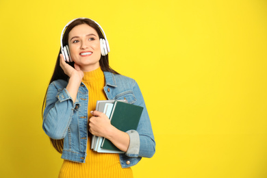 Young woman listening to audiobook on yellow background. Space for text