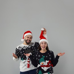 Happy young couple in Christmas sweaters and Santa hats on grey background