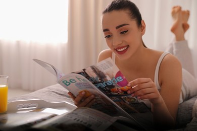 Photo of Happy woman reading magazine on bed indoors