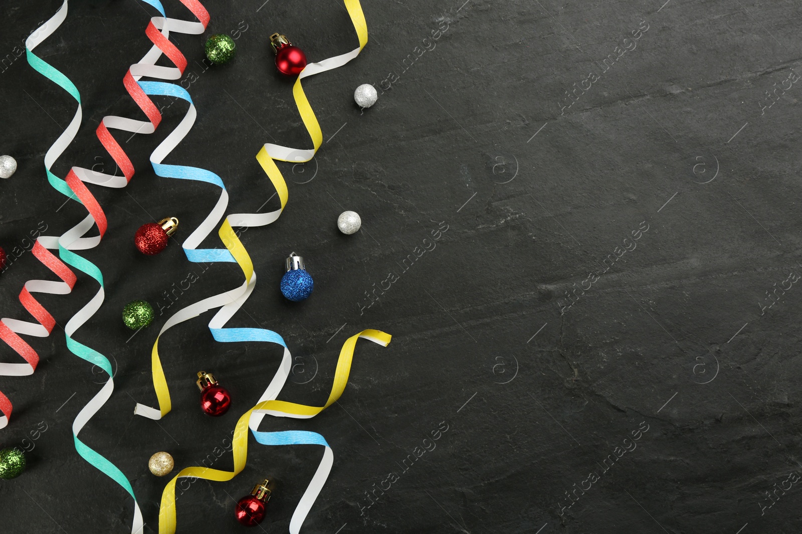 Photo of Colorful serpentine streamers and Christmas balls on black background, flat lay. Space for text