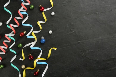 Colorful serpentine streamers and Christmas balls on black background, flat lay. Space for text