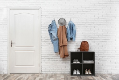 Photo of Stylish hallway interior with door, shoe rack and clothes hanging on brick wall