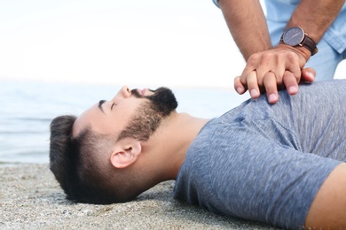 Photo of Passerby performing CPR on unconscious young man near sea. First aid