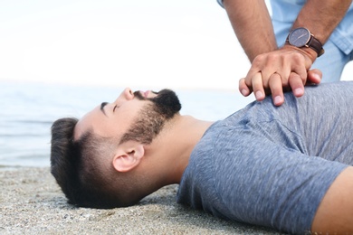 Passerby performing CPR on unconscious young man near sea. First aid