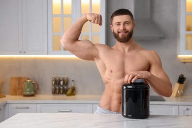 Young man with jar of protein powder at white marble table in kitchen, space for text