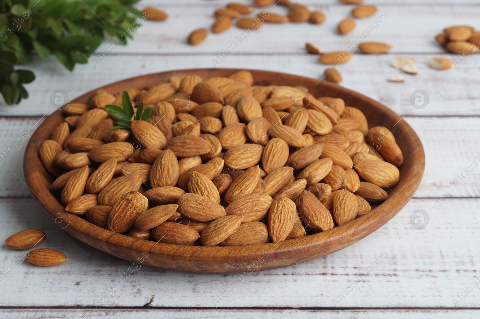 Photo of Plate with tasty almonds on white wooden table