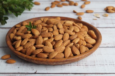 Plate with tasty almonds on white wooden table
