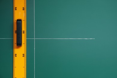 Photo of Ruler and cross drawn with chalk on green board, top view. Space for text
