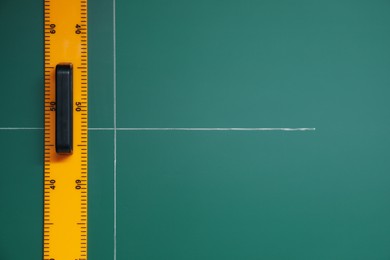 Ruler and cross drawn with chalk on green board, top view. Space for text