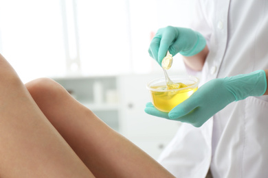Photo of Woman getting wax epilation of legs in salon, closeup