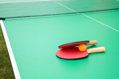 Photo of Rackets and ball on green ping pong table outdoors. Space for text
