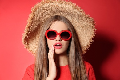Young woman wearing stylish sunglasses and hat on red background