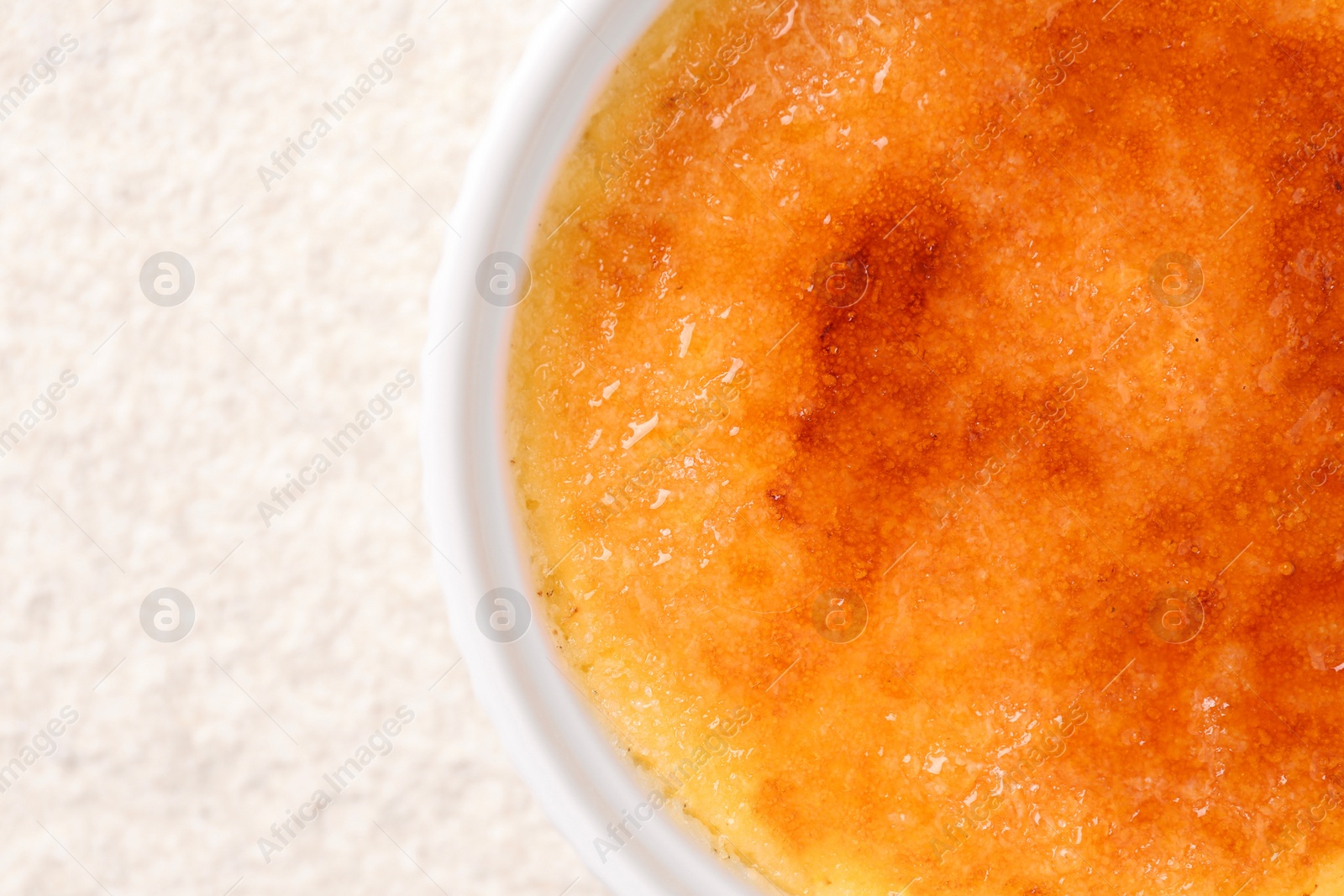 Photo of Delicious creme brulee in bowl on light textured table, top view. Space for text