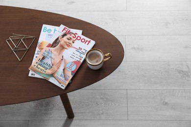 Magazines and cup of coffee on wooden table indoors, above view. Space for text