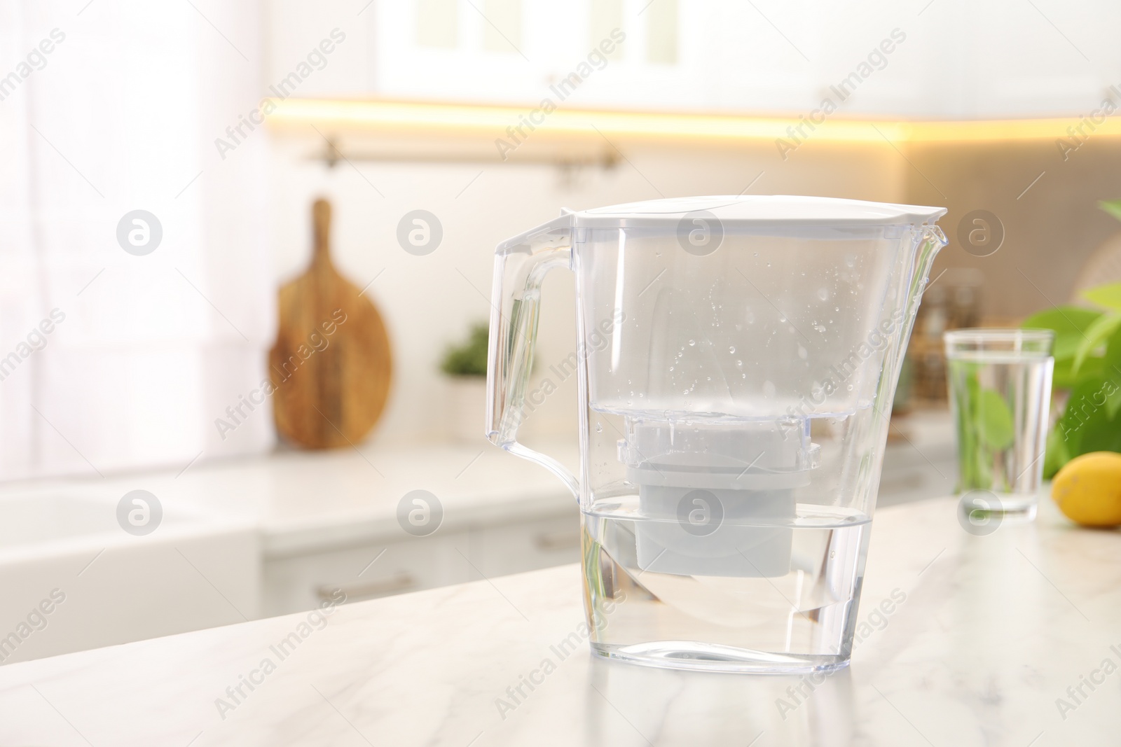 Photo of Water filter jug on white marble table in kitchen, space for text