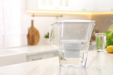 Water filter jug on white marble table in kitchen, space for text