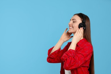 Photo of Happy woman in headphones enjoying music on light blue background, space for text